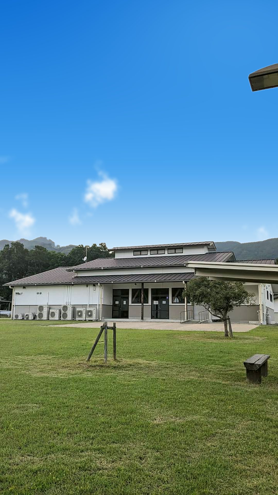青空の下に広がる里山ふれあい広場の芝生と、さとやま交流館